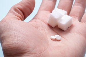 Paume d'une main avec du sucre et des pastilles d'édulcorant.